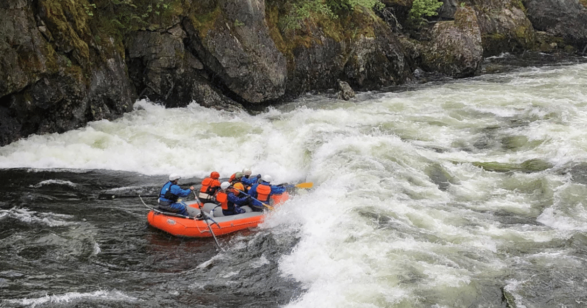 Adventurous whitewater rafting on the Lochsa River with Zoo Town Surfers. Rafters in bright safety gear paddle through turbulent rapids, surrounded by rocky cliffs and lush vegetation. The challenging waters highlight the excitement and skill required for this thrilling experience. Massive white water churns as the raft approaches it!